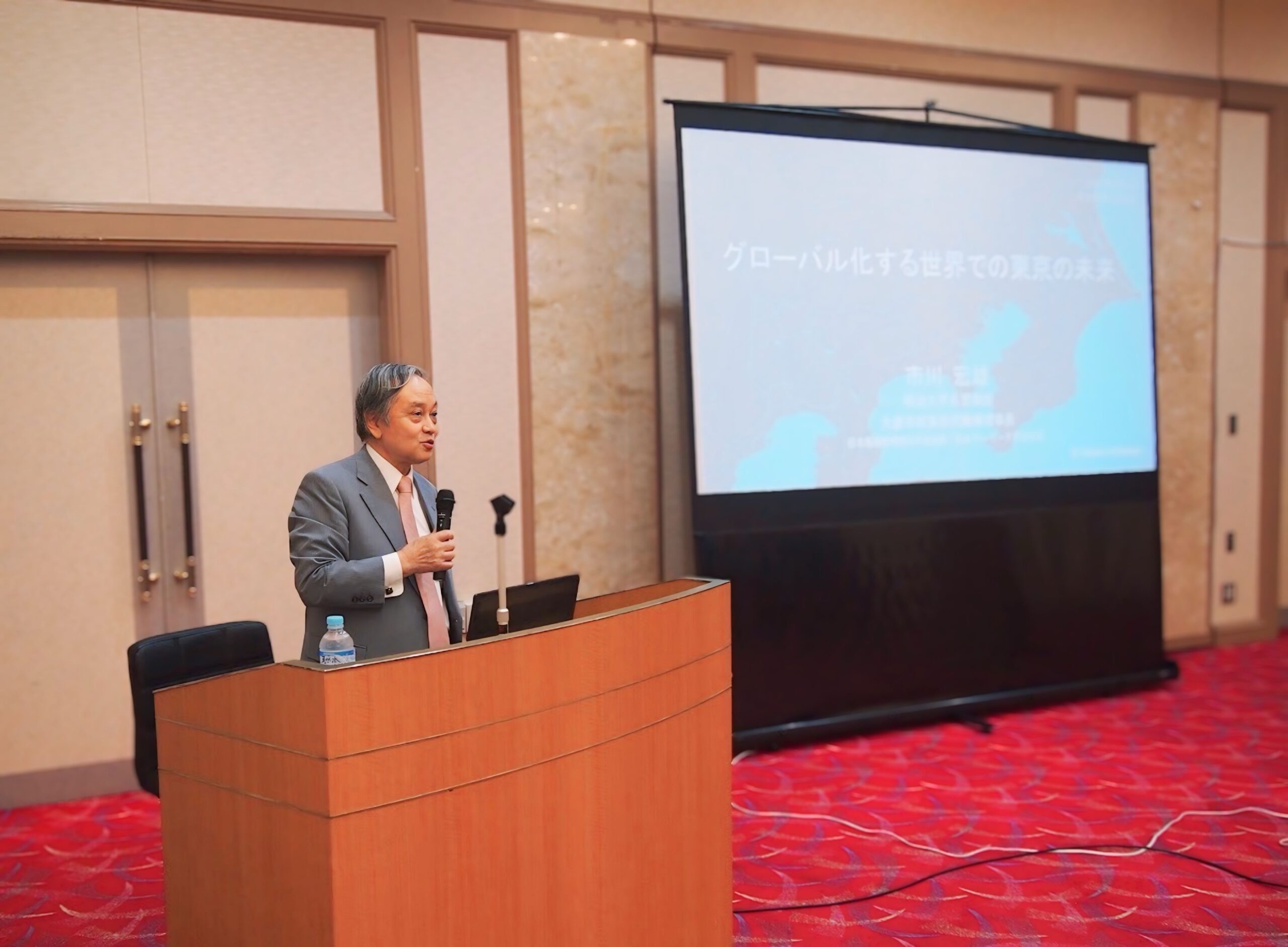 第7回交流会の講演で、スクリーンの横で話す参加者
